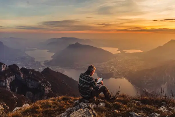 Man hiker solo on the mountain during golden hour reading e-book