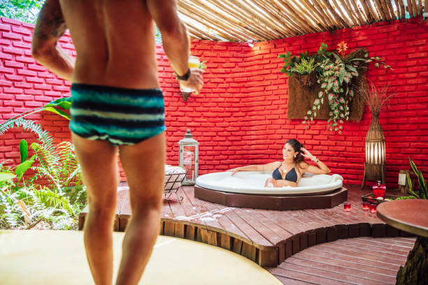 kobieta relaksująca się w wannie z hydromasażem mężczyzna brining napoje - swimming trunks bikini swimwear red zdjęcia i obrazy z banku zdjęć