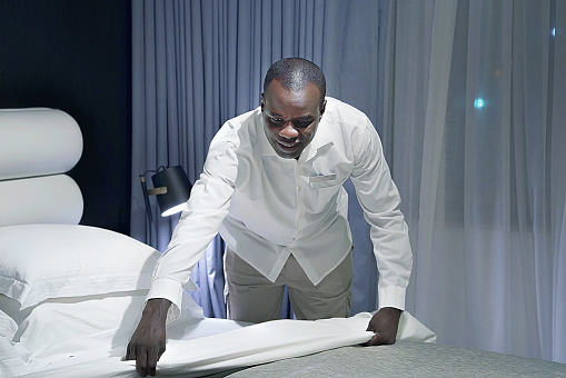 Maid making bed in hotel room. Staff Maid Making Bed. African housekeeper making bed. Toning