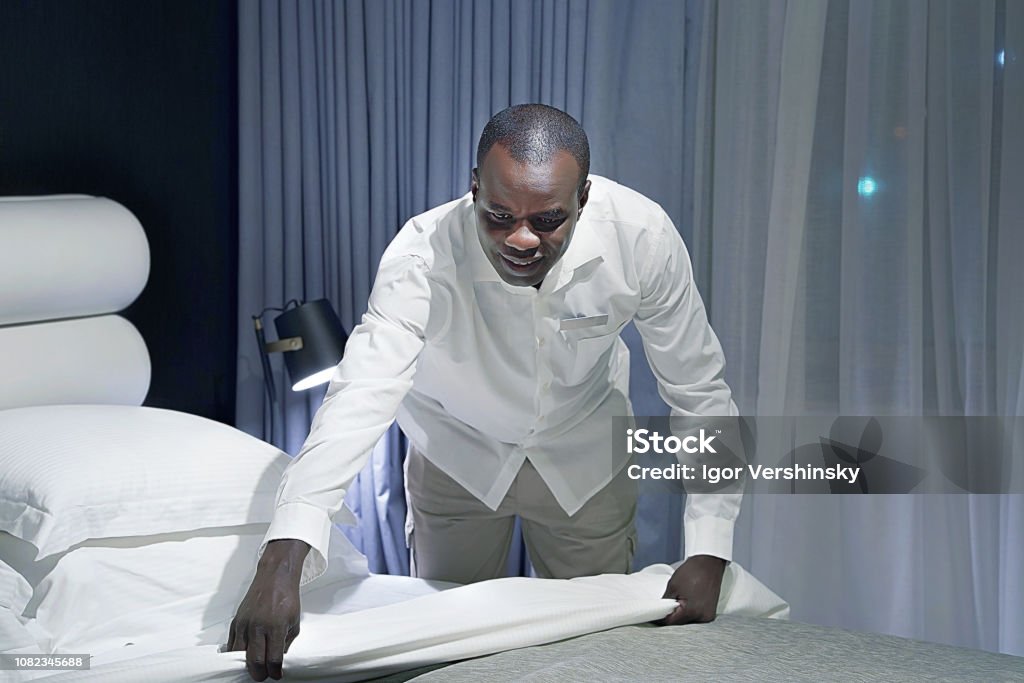 Maid Making Bed Maid making bed in hotel room. Staff Maid Making Bed. African housekeeper making bed. Toning Hotel Stock Photo