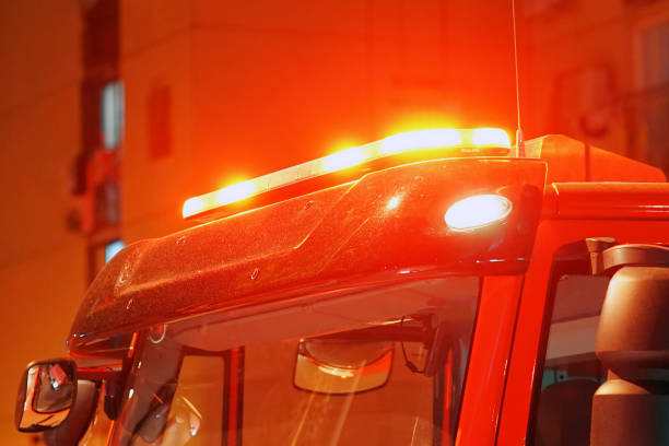 A Fire Engine in a small town parade with lights flashing. Blurred, out of focus to the point the details of the truck are not recognizable. Emergency lights visible.