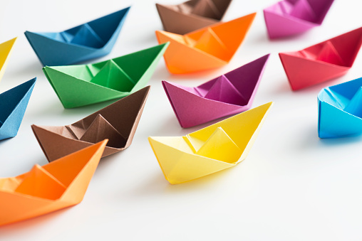 Multi coloured paper boats on white background.