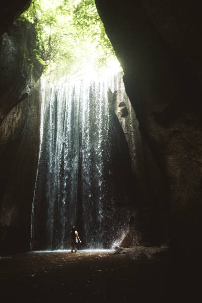 istock Woman staying under hidden waterfall in cave on Bali 1082357496