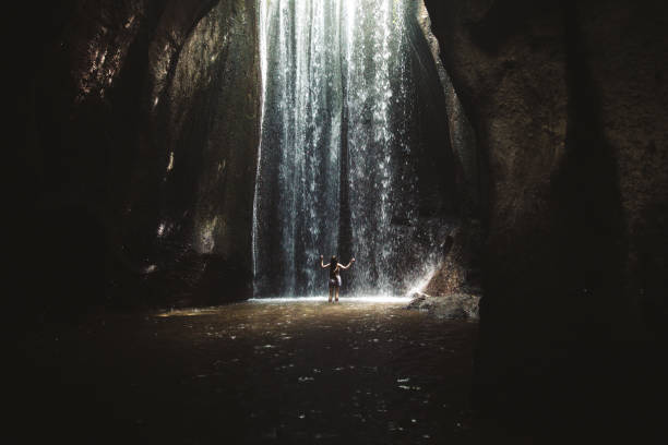 istock Woman staying under hidden waterfall in cave on Bali 1082357658