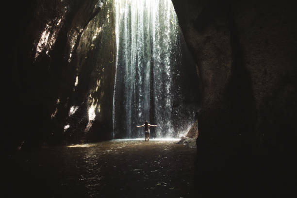 istock Woman staying under hidden waterfall in cave on Bali 1082357788