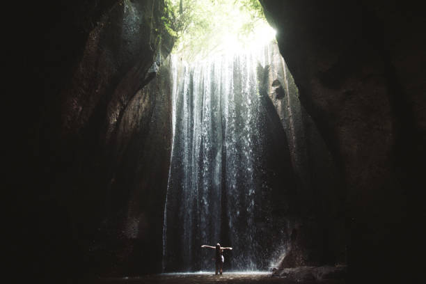 istock Woman staying under hidden waterfall in cave on Bali 1082359040