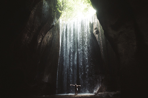 Woman enjoying sunrise at the cave washing under the beautiful hidden waterfall on Bali island in Indonesia