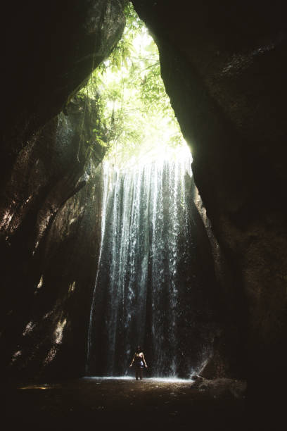 istock Woman staying under hidden waterfall in cave on Bali 1082359124