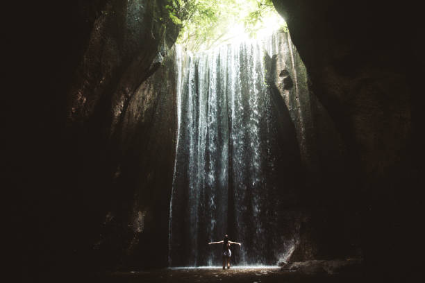 istock Woman staying under hidden waterfall in cave on Bali 1082359256