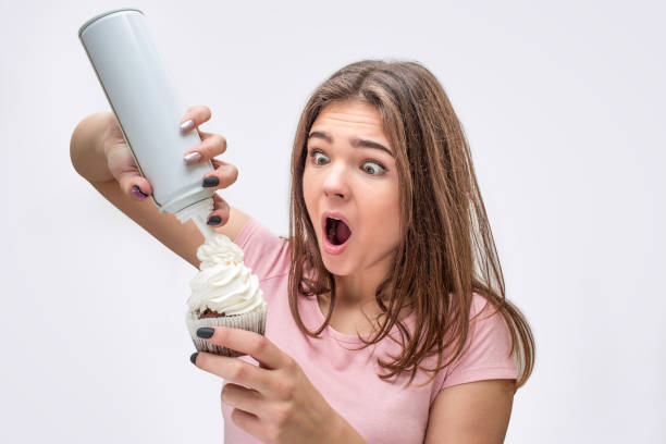istock Wondered young woman put some cream on cake. She keep mouth opened. Isolated on grey background. 1082362272