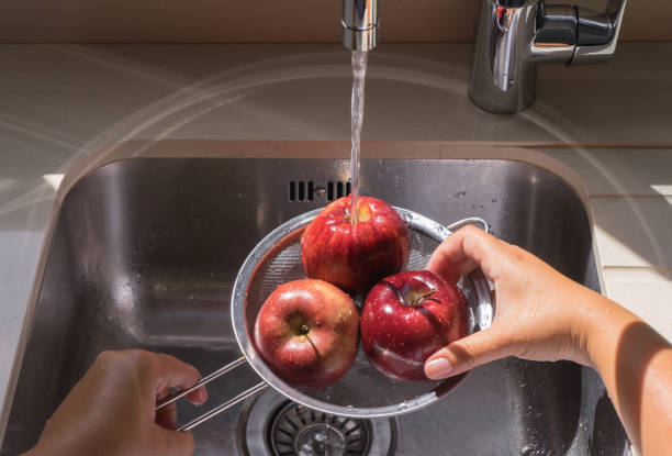 istock Female hands washing red apple in water stream 1082369416