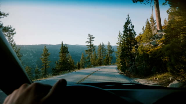 Beautiful first person view of male hand holding car steering wheel driving along mountain road in Yosemite slow motion.