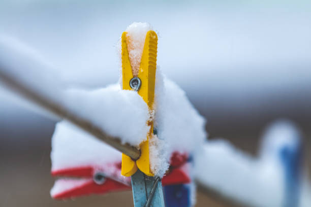 Colorful clips for washing laundry covered with snow on strip rope outdoor. Winter housework concept, close up, shallow depth of the field.