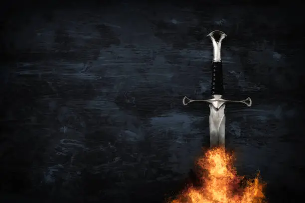 low key image of silver sword in the flames of fire. fantasy medieval period