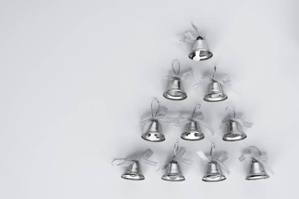 Silver bells arranged as a christmas tree on white background. Minimalistic greeting card with copy space for wishes.