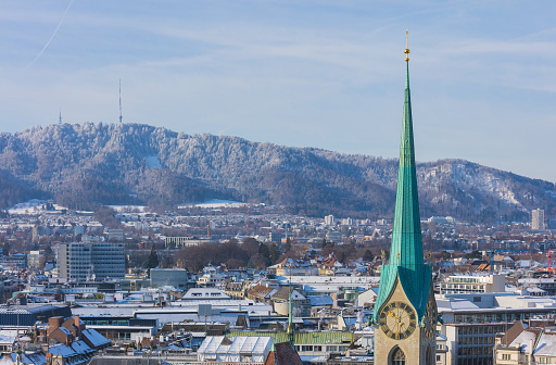 The city of Zurich in Switzerland as seen from the tower of the Grossmunster cathedral in winter, tower of the famous Fraumunster cathedral in the foreground., Mt. Uetliberg in the background.