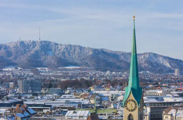 The city of Zurich in Switzerland as seen from the tower of the Grossmunster cathedral in winter, tower of the famous Fraumunster cathedral in the foreground., Mt. Uetliberg in the background.