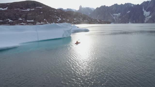 Aerial Shot Flying Over A Kayaker Towards Icebergs At Sunset - Side View