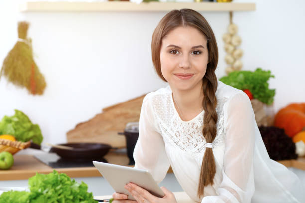 istock Young  woman using tablet while cooking or making online shopping in kitchen. Girl looking at the camera. Healthy lifestyle and vegan meal concepts 1082437112