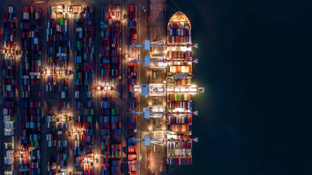 Photo of Crane shipping container at night, Aerial top view container ship carrying container import and export business logistic and transportation.