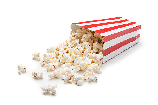 Front view of a red and white cardboard container laying down on white background with popcorn spilled out. Predominant colors are red and white. High key DSRL studio photo taken with Canon EOS 5D Mk II and Canon EF 100mm f/2.8L Macro IS USM.