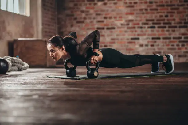 Fit female doing intense core workout in gym. Young woman doing push up exercise on fitness mat in health club.