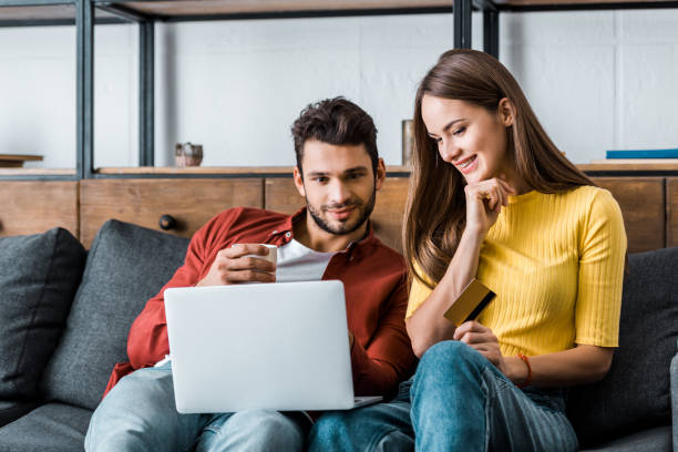 istock cheerful couple doing online shopping and smiling on sofa 1082471058
