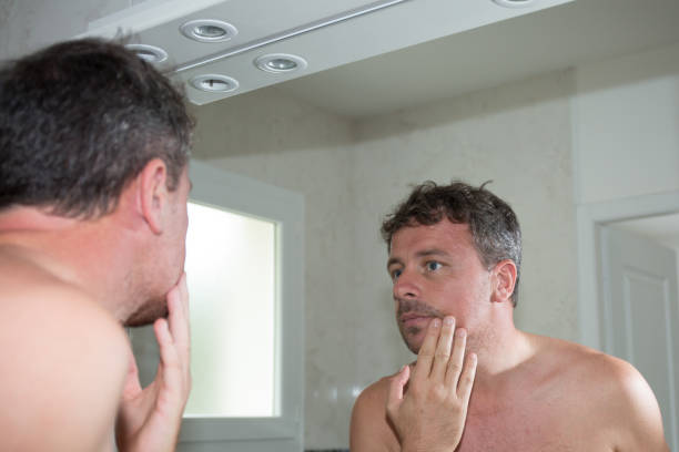 man in front of mirror looking at chin checking well-shaved - shaved head imagens e fotografias de stock