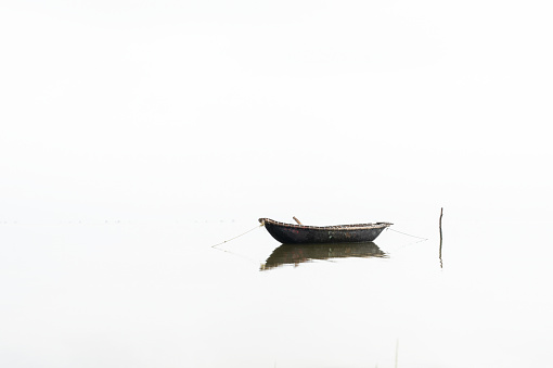 Traditional wooden fishing boat on a lake during sunrise, fog rising from water, Vietnam.