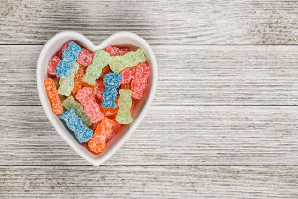 Sweet and Sour Candy Sugar Junk Food Variety of different color sweet and sour candy or sugar junk food in a heart shaped bowl. sour taste stock pictures, royalty-free photos & images