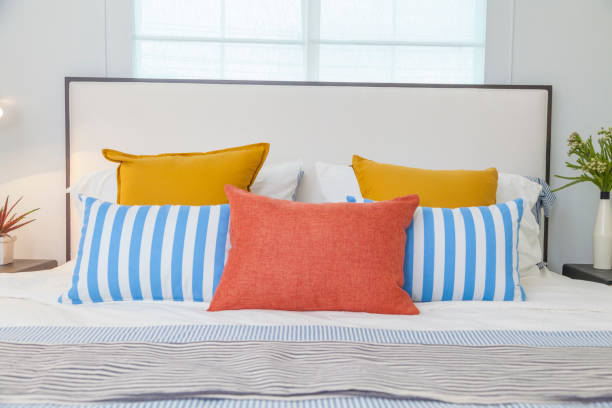 istock orange, yellow and blue pillows on white bed at home 1082484280