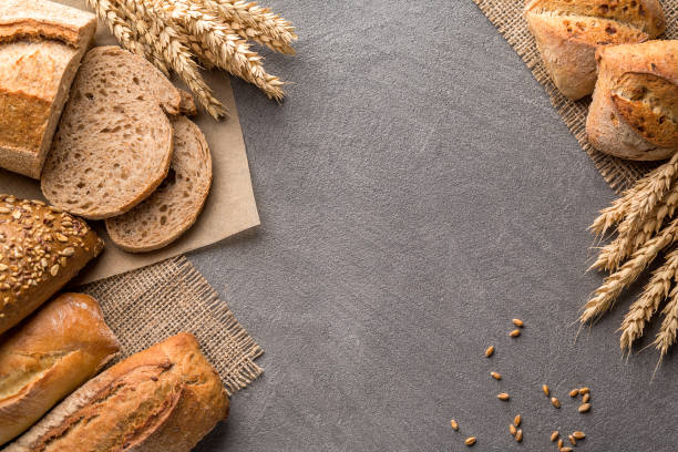 istock Bread background with wheat, aromatic crispbread with grains, copy space, top view. Brown and white whole grain loaves still life composition with wheat ears scattered around. 1082487668
