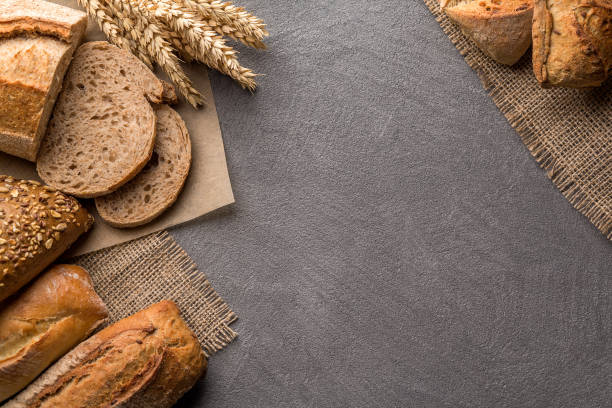 istock Bread background with wheat, aromatic crispbread with grains, copy space, top view. Brown and white whole grain loaves still life composition with wheat ears scattered around. 1082487676
