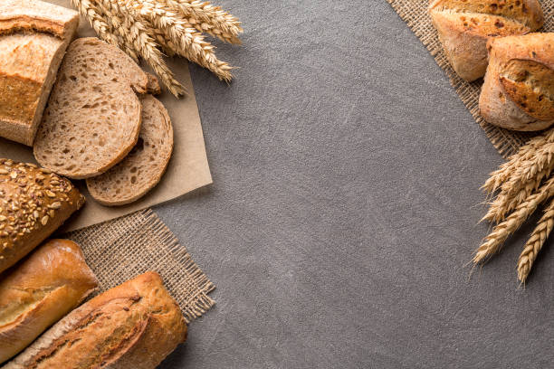 istock Bread background with wheat, aromatic crispbread with grains, copy space, top view. Brown and white whole grain loaves still life composition with wheat ears scattered around. 1082487736