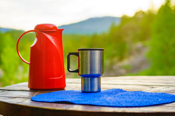 Picnic site table with thermos and thermal mug, norwegian mountains nature in the background. Camping with thermos.
