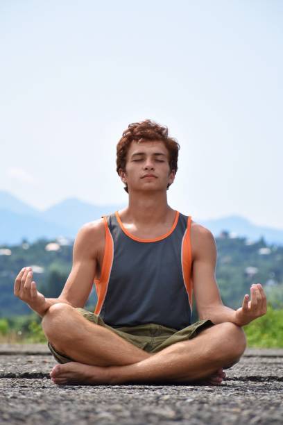 istock Young Man Meditating While Sitting On Footpath Against Sky 1082510264