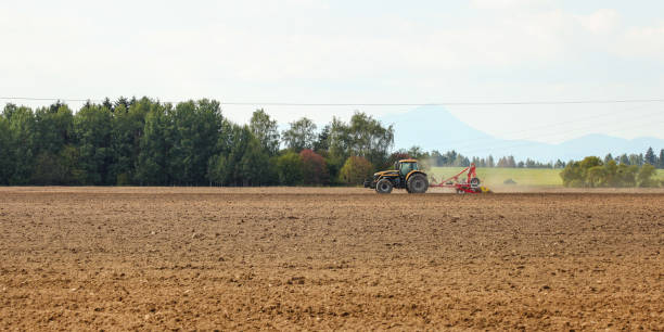istock Tractor sowing in empty field on countryside with some mountains in background. 1082518808