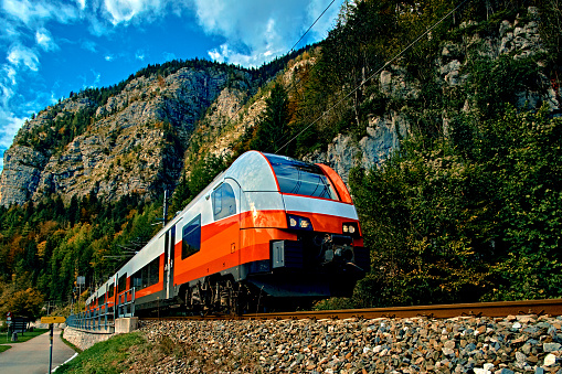 Red blue train in motion in Austrian alps mountains. High speed mountain train arrives at Hallstatt Obertraun train station in mountains. Location: resort village Hallstatt, Salzkammergut, Austria.