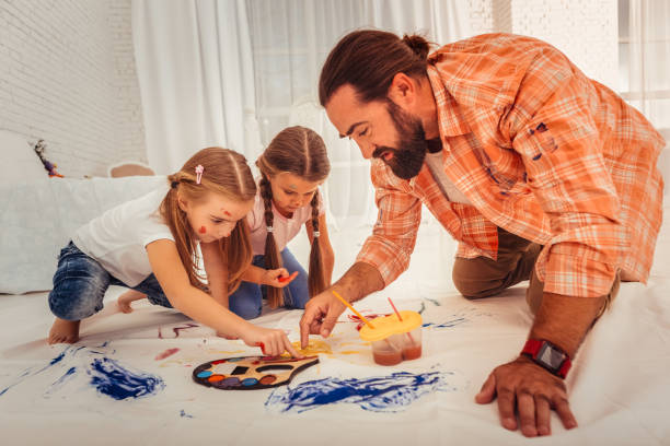 istock Nice bearded man teaching girls to paint on cloth 1082577406