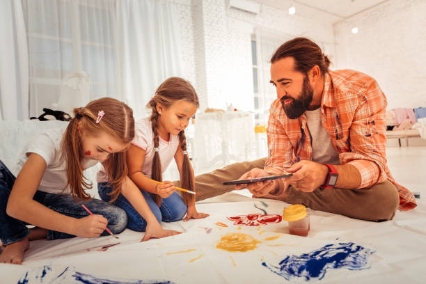 istock Nice bearded man helping his girls to paint 1082577472