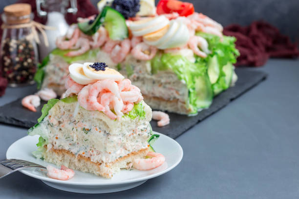Piece of traditional savory swedish sandwich cake Smorgastorta with bread, shrimps, eggs, caviar, dill, mayonnaise, cucumber and lettuce, horizontal, copy space stock photo