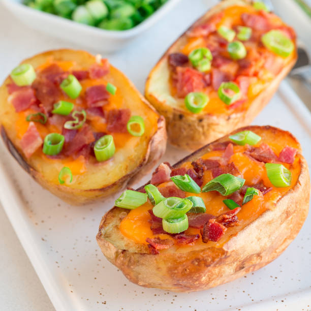 istock Baked loaded potato skins with cheddar cheese and bacon on ceramic plate, garnished with scallions and sour cream, square format 1082584100