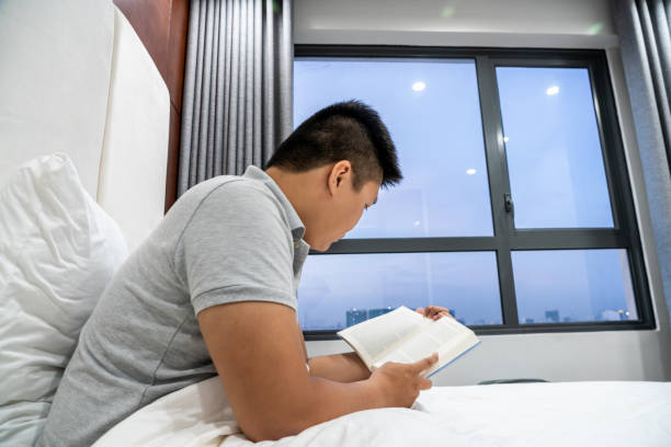 istock Side view of young man reading book on bed 1082638606