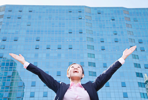 Chinese businesswoman with arms outstretched in front of skyscraper