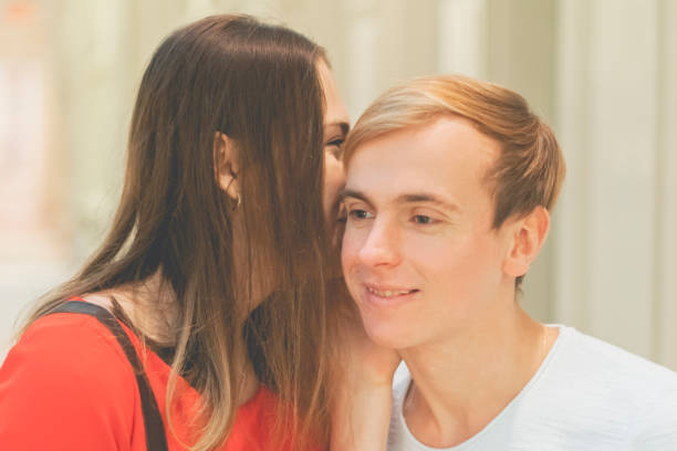 mujer joven comparte un secreto con su novio en el oído cerca a f retrato - whispering couple discussion smiling fotografías e imágenes de stock