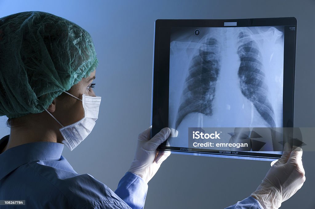 Feminino médico usando uma máscara olhando no raio-X - Foto de stock de Imagem de raios X royalty-free
