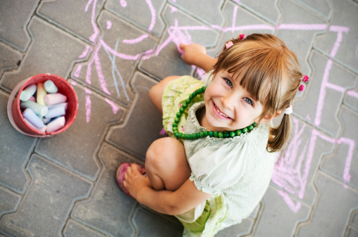 A little girl drawing on a sidewalk with chalk.