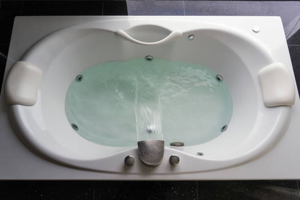Empty white massaging jetted bathtub on black polished stone floor stock photo