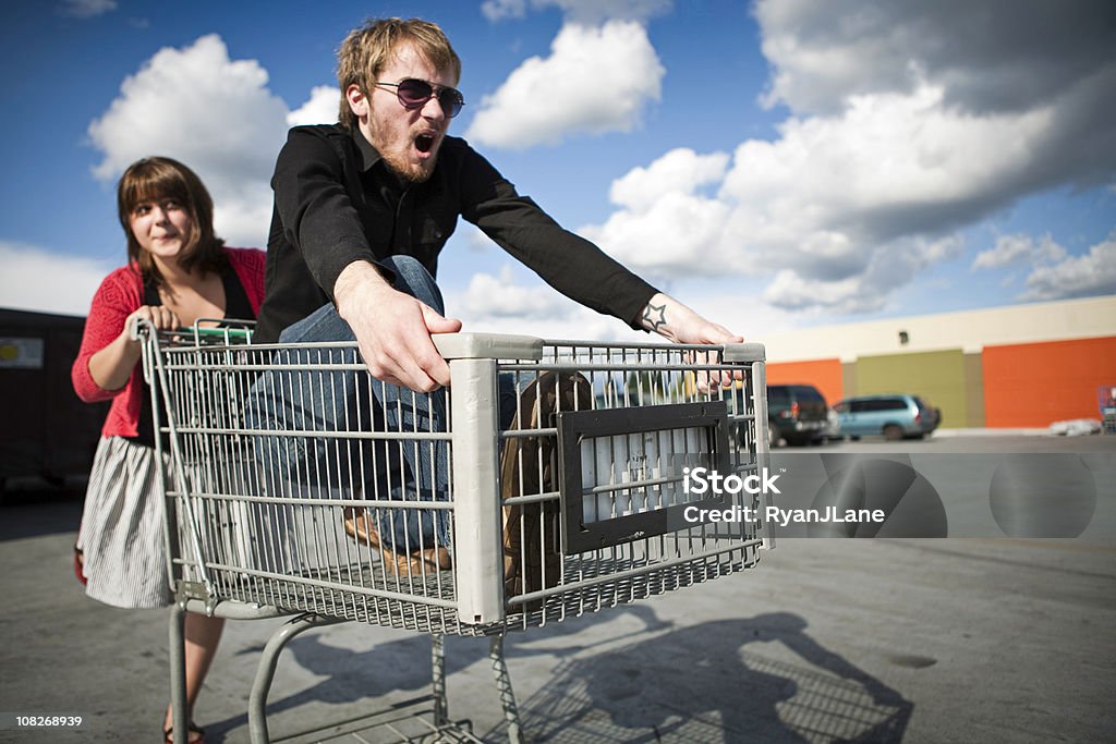 Giovane Coppia nel carrello acquisti corsa - Foto stock royalty-free di Carrello della spesa