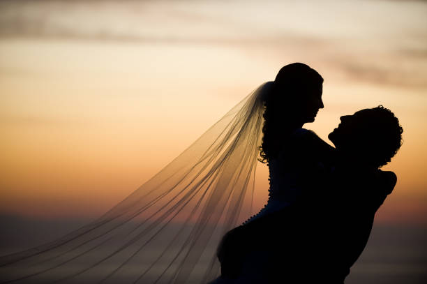 A wedding couple holding hands while standing in a garden against an amazing sunset.